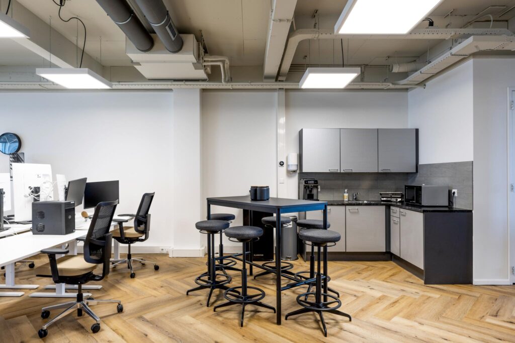 Moderne kantoorruimte aan de De Ruijterkade met werkplekken, een kitchenette en een hoge tafel met krukken.
